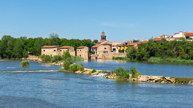 Scenic view of historic river village with stone buildings water mill dam and church tower under blue sky, City of Zamora in Spain, castile and Leon