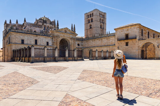 Woman tourist with hat standing on square looking at historic European cathedral rear view summer travel, Zamora Cathedral in Spain