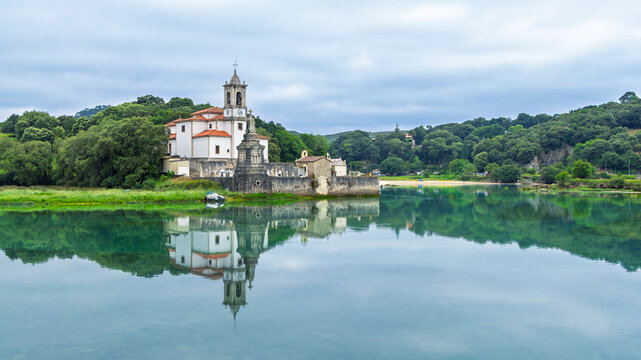 Historic church with graveyard on coast reflecting in calm water under cloudy sky Niembro Asturias Spain