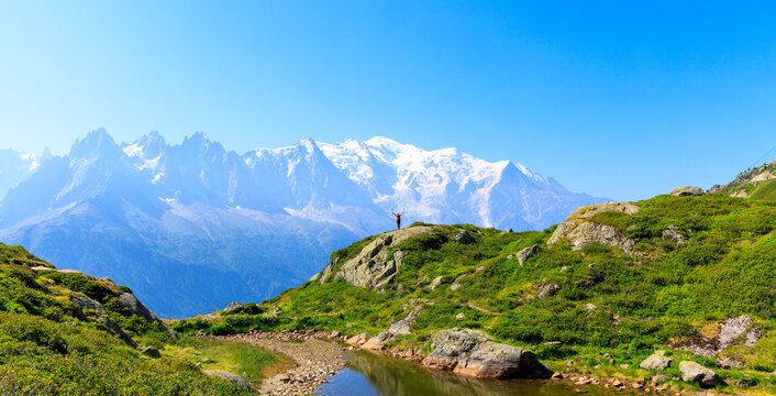 Hiker standing on mountain ridge with raised arms facing Mont Blanc snow peaks alpine landscape success freedom
