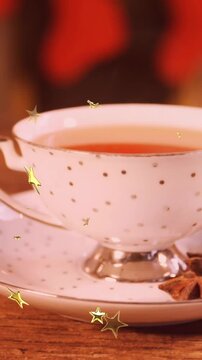 Animation of glowing stars falling over cup of tea with christmas cookies