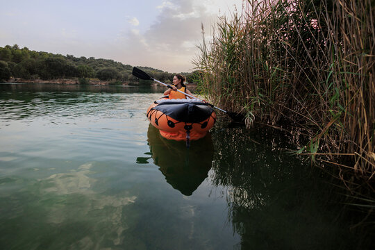 Woman paddling inflatable kayak on tranquil lake at sunset