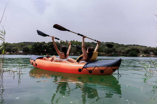 Young women celebrating success paddling inflatable kayak on lake
