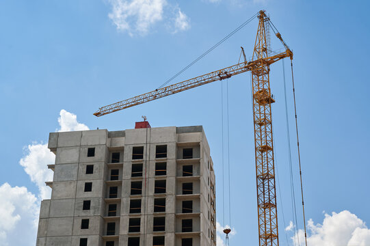 Tall yellow tower crane operating at a high rise building construction site against a blue sky