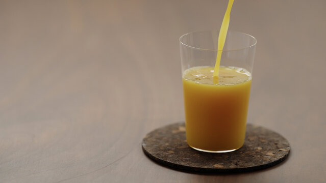 pour orange juice in a glass on a wood table