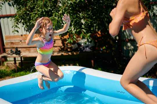 Two happy girls jumping into an inflatable swimming pool in the backyard on a sunny day