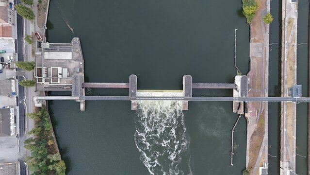 Aerial view of the Osthafen weir and lock system on the Main River with flowing water and industrial infrastructure in Frankfurt am Main, Hessen, Germany.