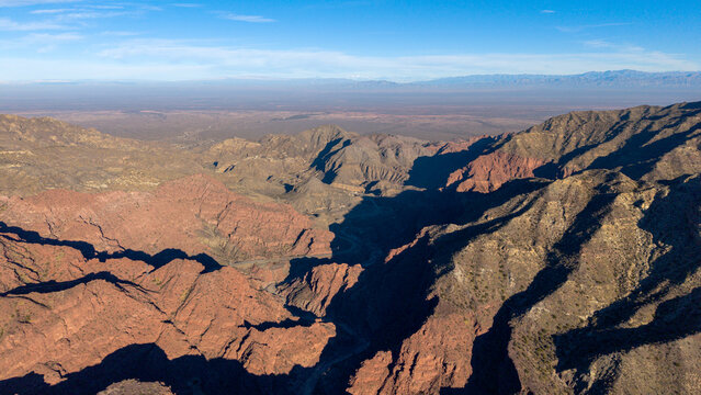 Aerial view of Ruta Nacional 150 winding through the rugged, arid canyons and reddish rock formations of the mountainous landscape in San Juan, Argentina.