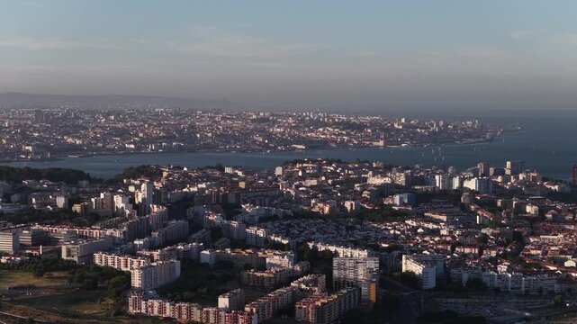 Sweeping aerial footage captures Lisbon's cityscape, Tagus river, and Almada in golden evening light. Modern buildings, winding streets, and shimmering water highlight Portugal's vibrant urban charm.