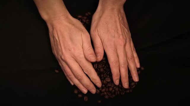 Top down shot of hands touching and handling coffee beans against a black backdrop