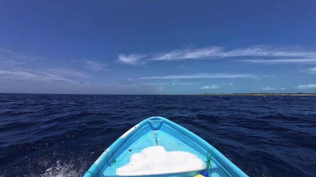 Bow of small fishing boat moves through blue Caribbean sea near distant coastline