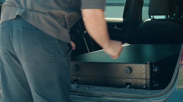 Shot of a man lifting a metal utility cart into the back of a vehicle before walking away in a workshop setting