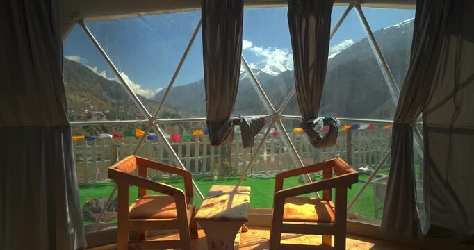 Annapurna Circuit, Manang, Nepal, a luxury glamping tent showing two wooden chairs and a table framing panoramic views of snow-capped Annapurna peaks.