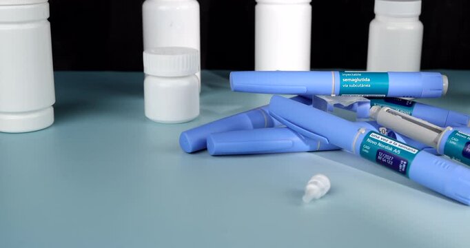 Horizontal traveling camera movement sliding across blue Semaglutide GLP-1 pens and white pill bottles on a light blue table against a black background, diabetes therapy layout concept