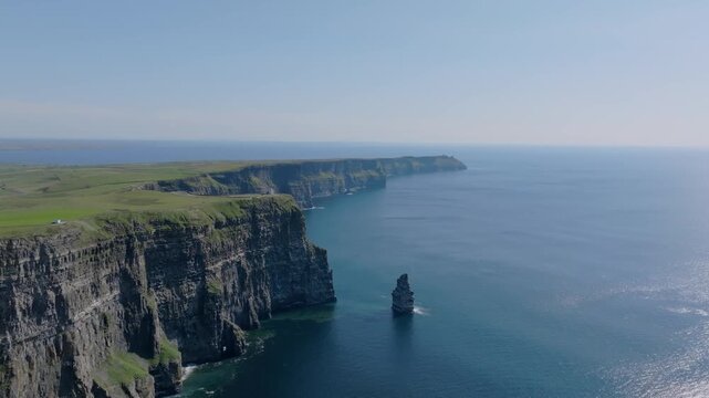 Steep grass-topped cliffs and a lone sea stack edge the calm Atlantic as the camera flies gently along the Moher coastline.