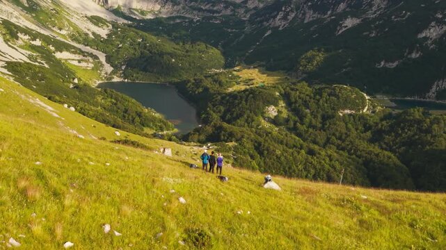 Drone shot pulling back from hikers to reveal majestic Skrcka Valley, Bobotov Kuk, and glacial lakes in Durmitor National Park, Montenegro