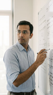 Focused businessman writing strategy diagram on office whiteboard carefully