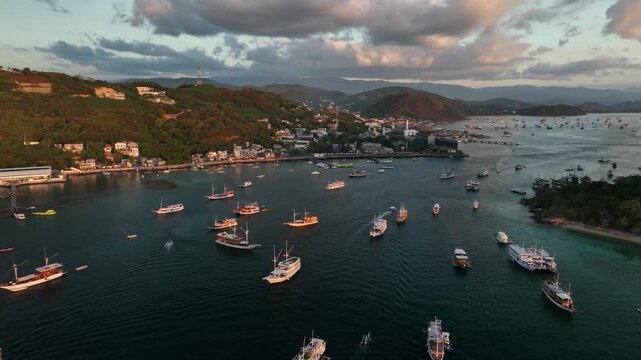 Aerial view of Labuan Bajo harbor with numerous boats anchored in the bay during golden hour in Komodo, East Nusa Tenggara, Indonesia.