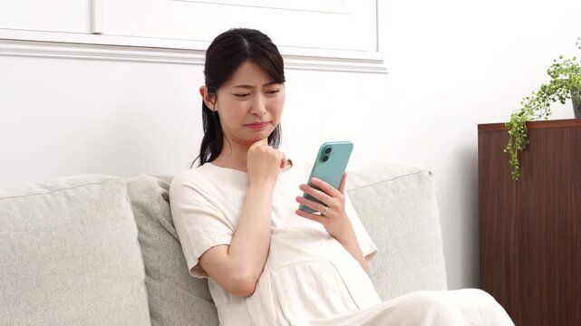 リビングで不安な表情でスマホを見る妊婦