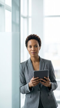 Confident businesswoman holding a digital tablet by a bright office window