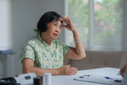 Elderly Asian woman experiencing headache during medical consultation