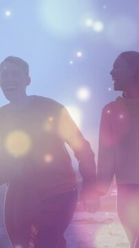Animation of glowing spots of light over african american couple walking on the rocks near the sea