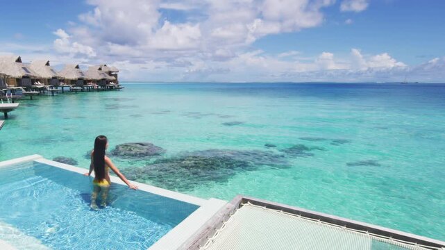 Luxury resort travel vacation idyllic overwater bungalow villa woman relaxing by pool. Social media influencer traveler luxurious high end lifestyle. Raw unedited video of real unretouched woman