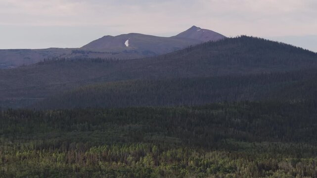 Aerial of Uinta Mountain landscape over forest in Summit County Utah in summer with rugged ridge line and patch of snow