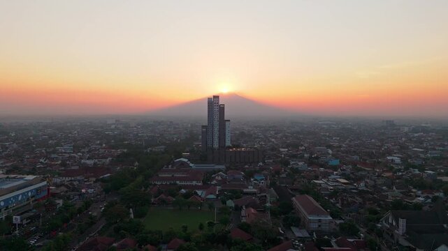 Aerial view of the modern building silhouette against the backdrop of Mount Merbabu during a vibrant sunset in Surakarta, Central Java, Indonesia.