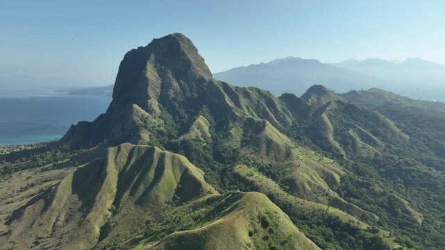 Aerial view of the rugged Nuca Molas mountain with lush green slopes and coastal scenery in Satar Mese Barat, East Nusa Tenggara, Indonesia.
