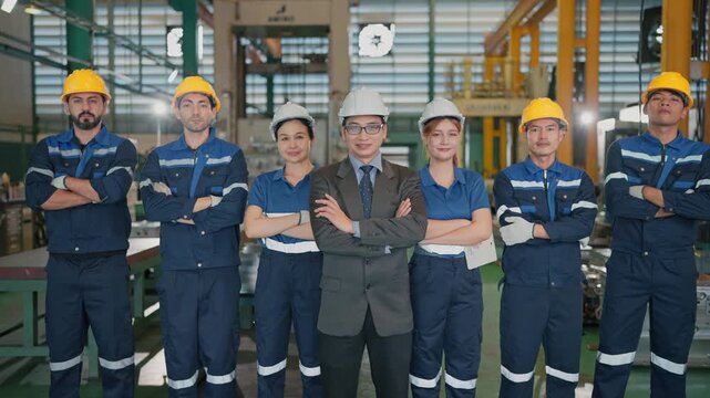 Group workers stand confidently in a factory. Man in a suit stands center, arms crossed. They wear hard hats and uniforms, showing pride