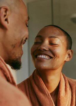 Close-up of a man and a woman in a bathroom. the man is on the left side of the image, facing the woman, and they are both wearing orange bathrobes.