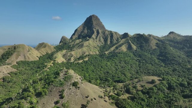 Aerial view of Nuca Molas peak rising above lush green hills and tropical vegetation in Satar Mese Barat, East Nusa Tenggara, Indonesia.