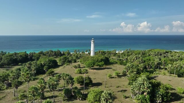 Aerial view of the Nuca Molas lighthouse surrounded by palm trees and coastal vegetation overlooking the blue sea in Satar Mese Barat, East Nusa Tenggara, Indonesia.
