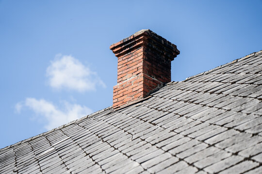 Vintage clay brick chimney pot on an weathered slate roof structure under clear blue sky concept of residential heating systems
