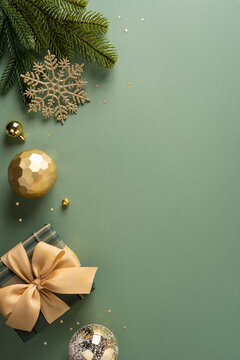 Merry Christmas and Happy New Year greeting with wrapped gift, golden ornaments and fir branch on vertical olive color background