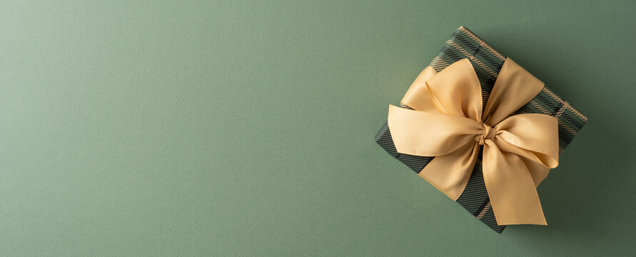 Elegant wrapped Christmas gift with gold bow on green background for holiday celebration