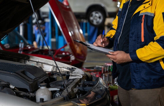 closed up mechanic in workwear writing paper on clipboard after inspection of a car engine that needs to be repaired in order to provide a quotation to customer