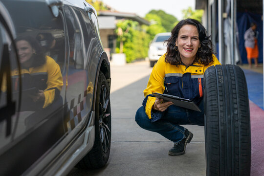 smiling female mechanic holding clipboard and inspecting a car tire at auto repair shop