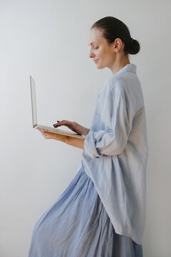 Female Model Typing On Laptop In Casual Light Blue Shirt Against Plain White Wall