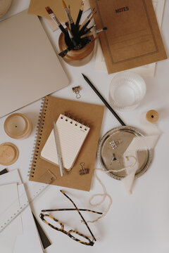 Aesthetic Neutral Workspace Table Arranged With Notebooks, Glasses, Paintbrushes, And Silver Tray