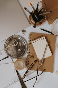 Minimalist Artist Workstation Essentials Including Spiral Notebook, Silver Pen, Candle, And Ruler