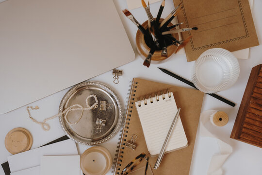 Top View Cozy Artist Workspace Arranged With Kraft Journals, Silver Tray, Pearl Necklace, And Candle