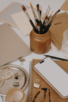 Blank Mobile Screen Mockup Resting On Kraft Notebook In Neutral Artist Studio Desk Setup