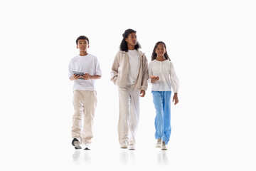 Fototapeta premium Three young friends walking together in casual outfits on white background. Concept of youth lifestyle, friendship community, generation culture.
