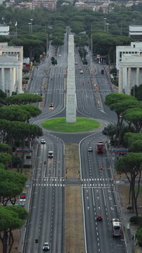 Aerial view of the iconic Obelisco Marconi standing in the center of a wide road in the EUR district surrounded by pine trees in Rome, Lazio, Italy.