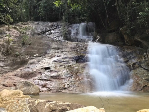 Beautiful tropical waterfall flowing over rocky terrain into a natural pool surrounded by lush rainforest, creating a refreshing wilderness scene.