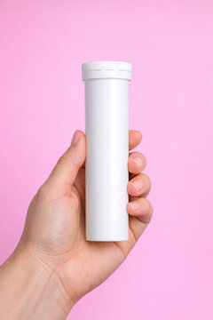 Pharmacy pill bottle with blister pack cap for medication, held by hand in pink background.