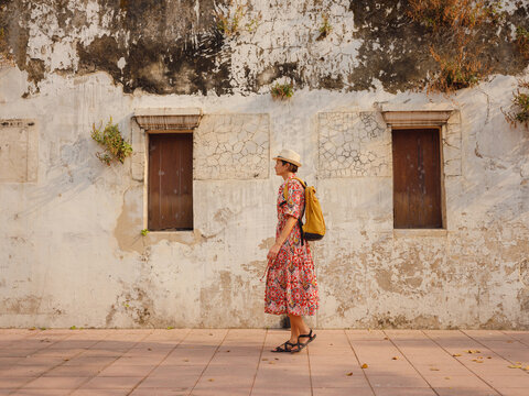 Young female tourist walks through historic Lhong 1919 courtyard in Bangkok Chinatown. Woman enjoys heritage Chinese architecture, ancient brick buildings, and cultural atmosphere.