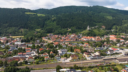 Fototapeta premium Summer drone footage showing medieval Friesach, old fortified walls, rooftops, towers, hills, serene atmosphere, warm daylight, gentle cinematic motion